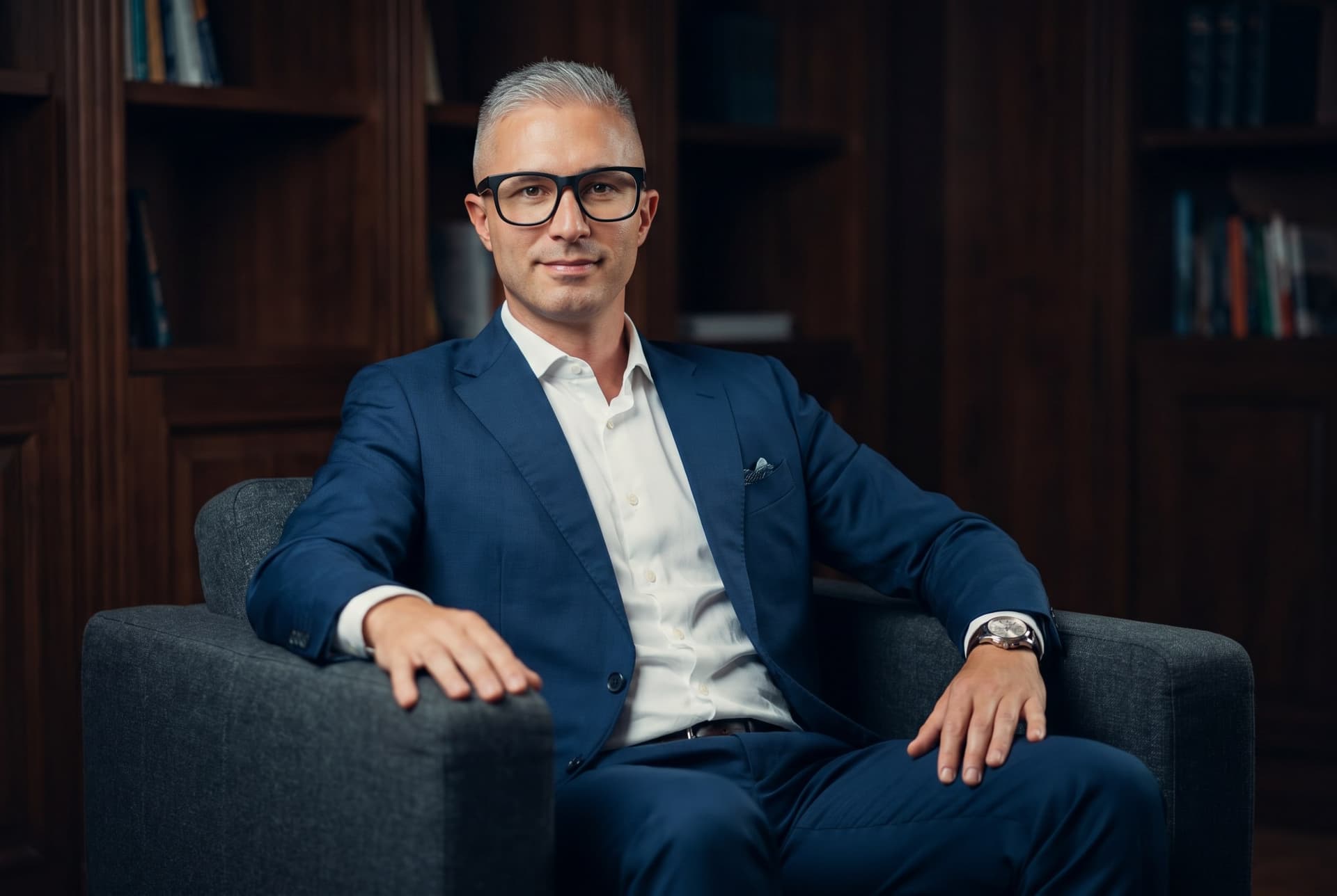 Guido Möller im blauen Anzug sitzend vor einer Bücherwand aus dunklem Holz